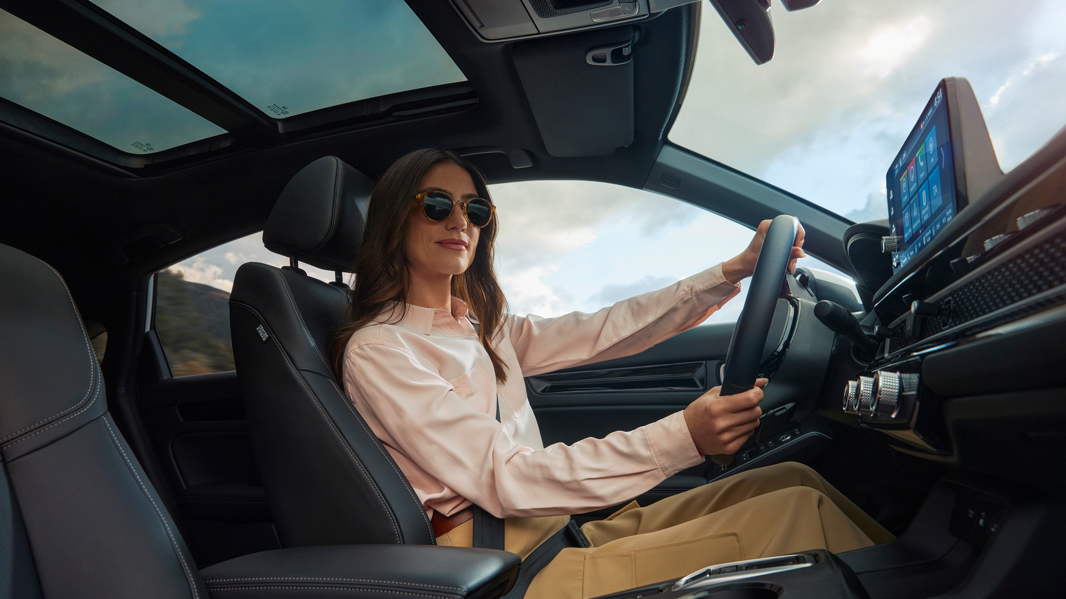 Una donna con occhiali da sole, con le mani sul volante della Civic Hybrid